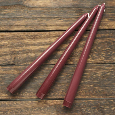 Three burgundy colored candles on a wooden surface.