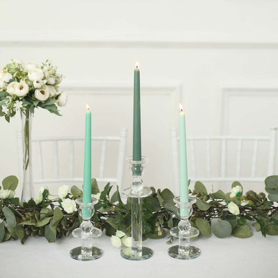 Three elegant candles in glass holders on a decorated table with greenery and flowers.