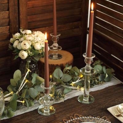Elegant glass candle holders with brown candles on a rustic table setting.