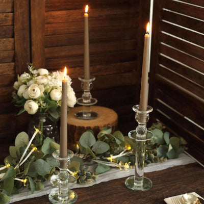 Elegant glass candle holders with lit candles and greenery arrangement.