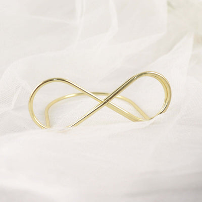 Gold infinity bracelet on soft fabric backdrop.