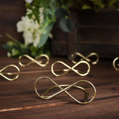 Gold infinity loop decor accents on wooden surface with greenery backdrop.