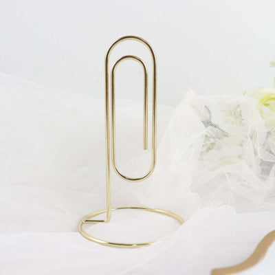 Gold paperclip holder on soft white fabric backdrop.