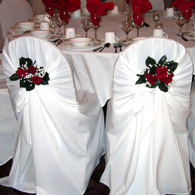 Elegant white chair covers with red floral accents at a beautifully set dining table.