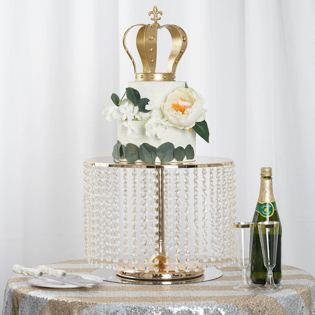 Elegant crown cake with floral accents on a crystal stand, champagne, and glasses.