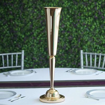 Elegant gold vase centerpiece on a dining table with greenery backdrop.