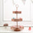 Three-tiered rose gold cake stand with decorative cutouts and macarons on top.