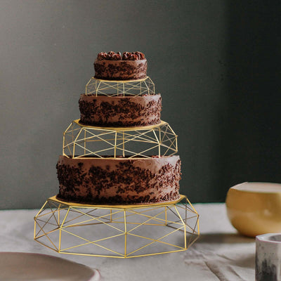 Four-tiered chocolate cake with geometric gold stand on a table.