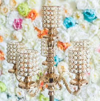 Elegant gold chandelier with pearl candle holders against a colorful floral backdrop.