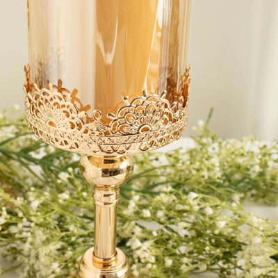 Elegant gold candle holder with intricate lace design, adorned with greenery.