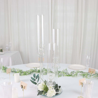 Elegant glass candle holders with greenery and floral accents on a table setting.