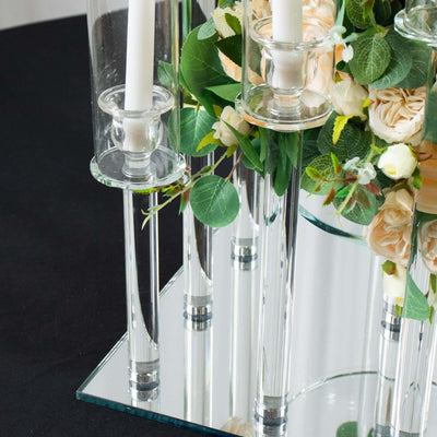 Glass candle holders with floral arrangement on a mirrored surface.