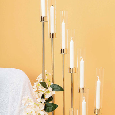 Modern gold candle holder with glass tubes and white candles against a yellow background.