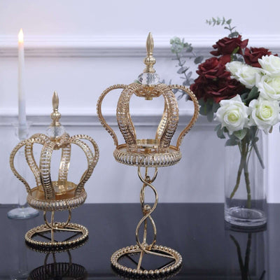 Gold crown-shaped candle holders on a table with flowers and a candle.
