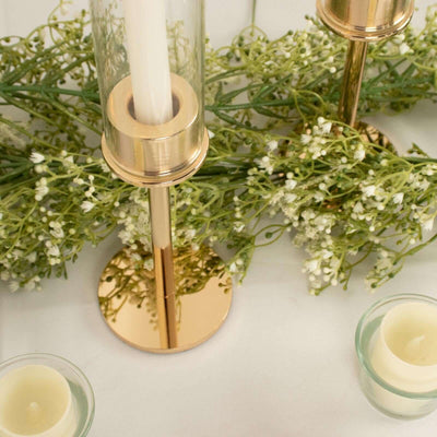 Gold candle holders with greenery and candles on a white surface.