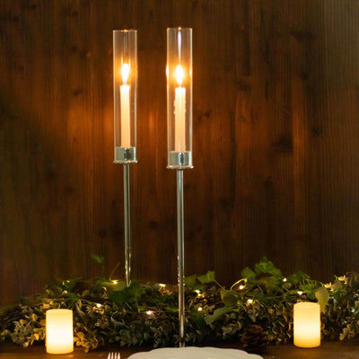 Elegant candle holders with glowing candles and greenery backdrop.