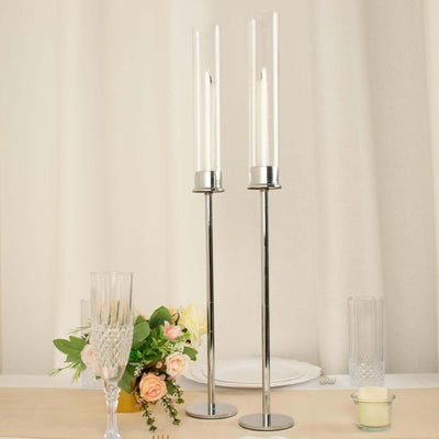 Elegant tall candle holders with glass cylinders and silver bases.