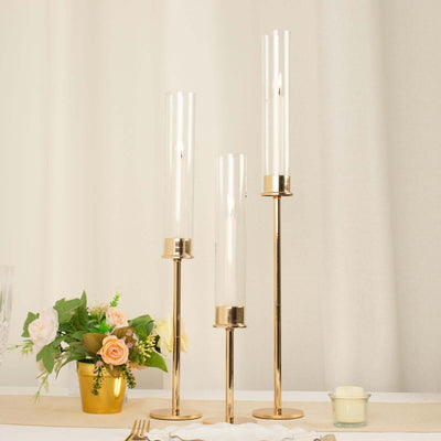 Elegant gold candle holders with glass cylinders, perfect for dining decor.