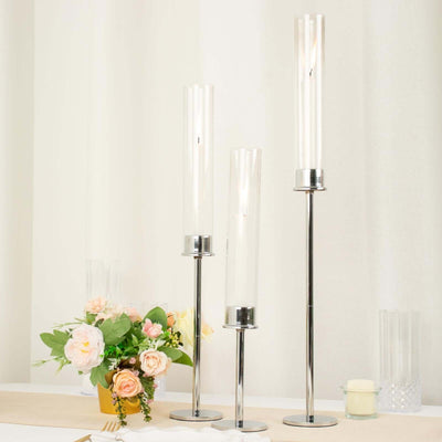 Elegant candle holders in varying heights with floral arrangement on a table.