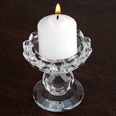 White candle in a crystal holder with flame on dark wooden surface.