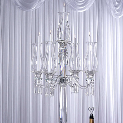 Elegant crystal chandelier with candle-like lights against a draped backdrop.