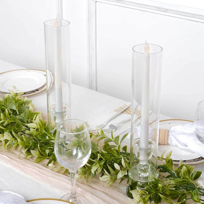 Elegant table setting with glass candle holders and greenery centerpiece.