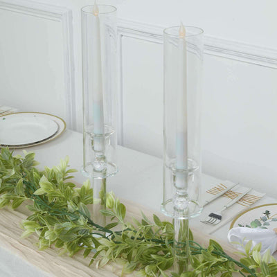 Elegant glass candle holders with white candles and greenery on a table setting.