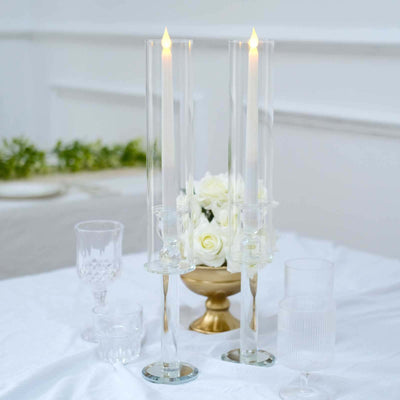 Elegant glass candle holders with lit candles and floral arrangement on a table.