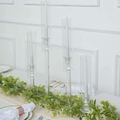 Elegant glass candle holders with white candles on a table with greenery.