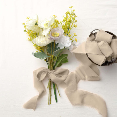 Bouquet of white and yellow flowers with a beige ribbon and fabric on a light backdrop.