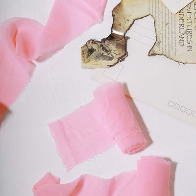 Pink fabric ribbons on a textured surface with vintage paper elements.
