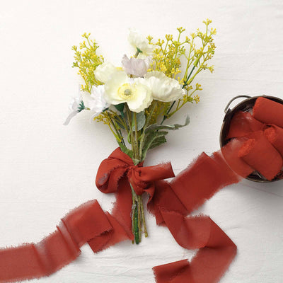 Floral bouquet with yellow and white flowers tied with a rust ribbon.