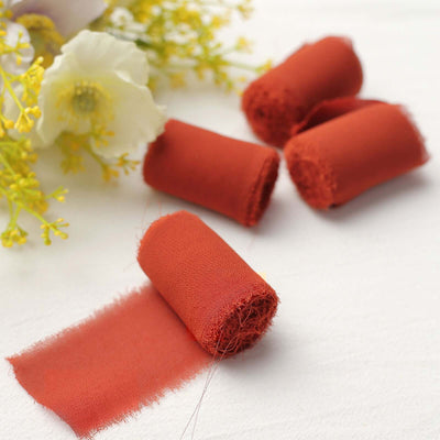 Rust-colored fabric rolls with frayed edges, surrounded by flowers.