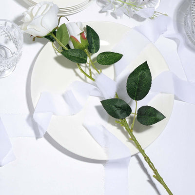 White rose and leaves on a plate with white fabric ribbons