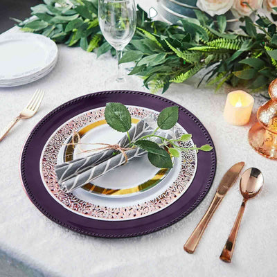 Elegant purple charger plate with gold trim, napkin, and greenery on a dining table setting.