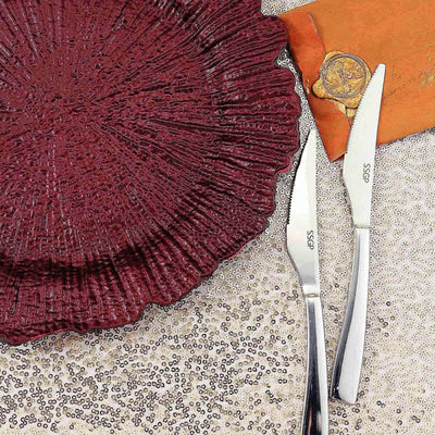 Elegant maroon plate with silver knives on a glittering tablecloth.