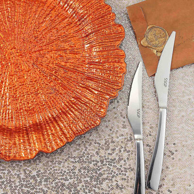 Orange textured plate with stainless steel knives on a sparkling background.
