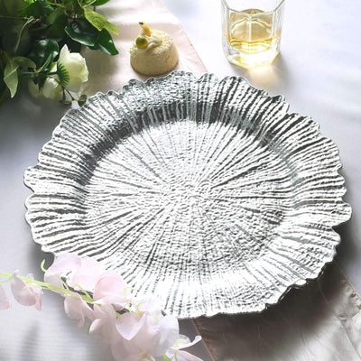 Textured silver serving platter on a table with floral accents and a drink.