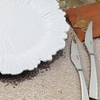 Elegant white plate with textured rim and silver knives on a sequined table setting.