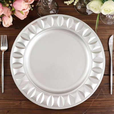 Silver decorative charger plate on a rustic wooden table with flowers and cutlery.
