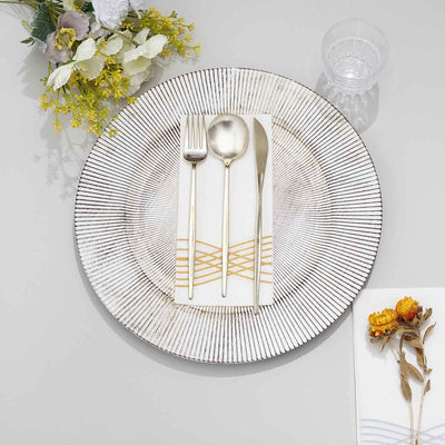 Elegant dinner plate set with gold-accented cutlery and napkins on a gray table.