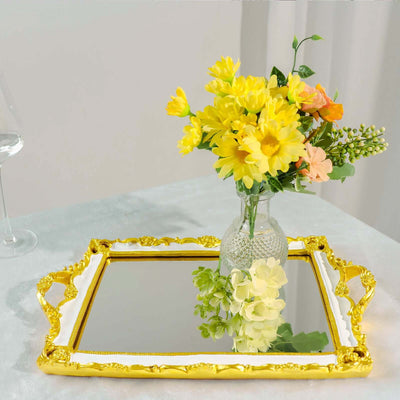 Decorative mirror tray with gold handles and vase of yellow flowers.