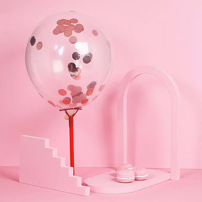 Pink balloon with confetti and macarons on a pink backdrop.