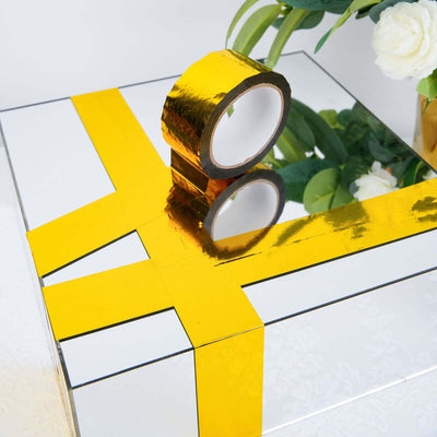 Mirrored gift box with gold ribbon and tape on a white surface.