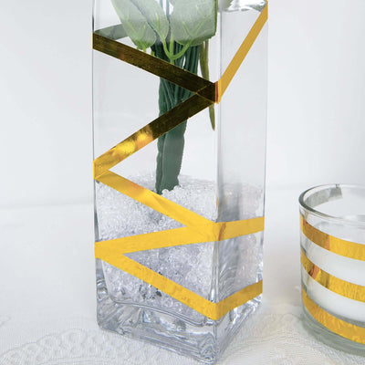 Glass vase with gold geometric design and faux plant, filled with decorative beads.