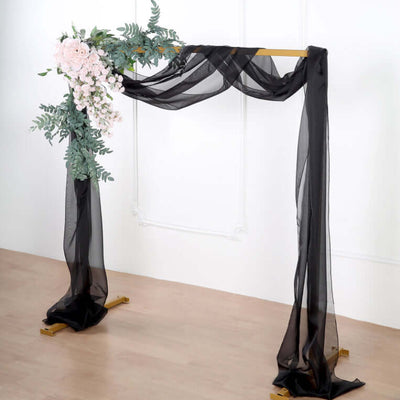 Black sheer fabric wedding arch with floral accents on a wooden base.