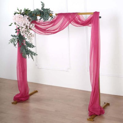 Floral arch decoration with pink drapes and greenery on a golden frame.