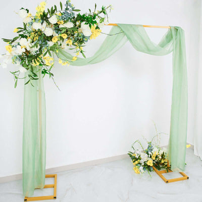 Floral wedding arch with green drapery and yellow blooms on a plain backdrop.