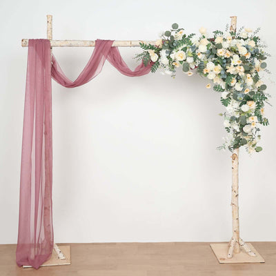 Floral wedding arch with draped fabric and greenery on a simple backdrop.