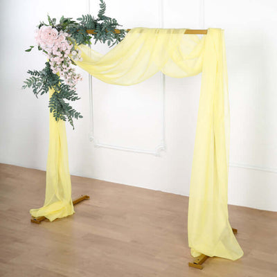 Yellow fabric wedding arch with floral accents and greenery on a neutral backdrop.
